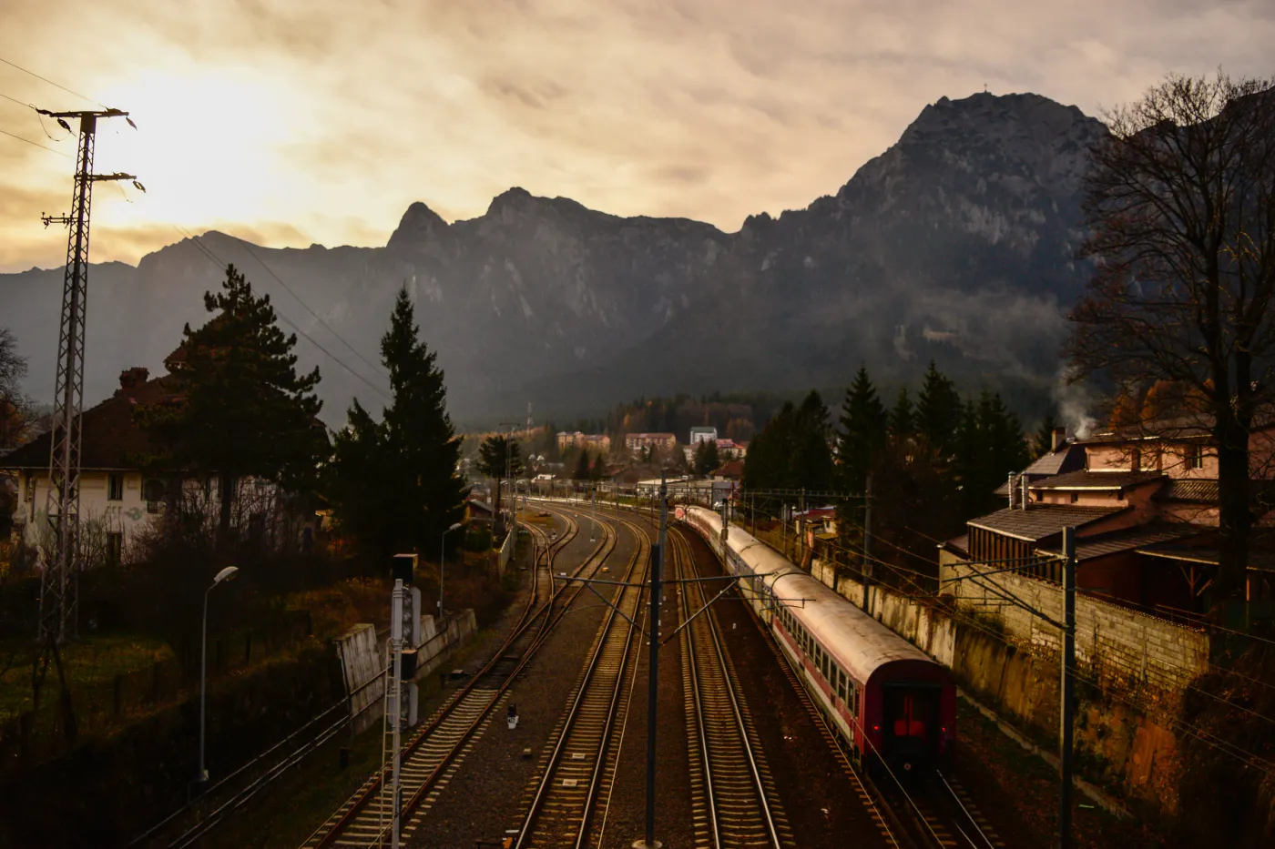 Railway tracks and a passenger train leading toward mountains under a luminous sky.