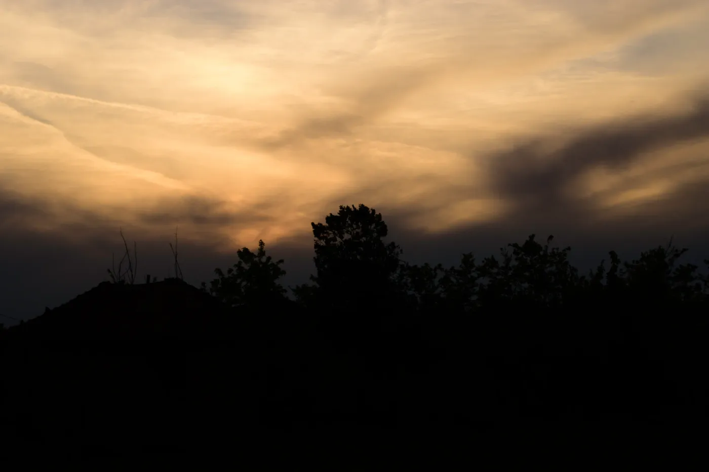 Dramatic golden evening clouds above a dark line of trees and rooftops.