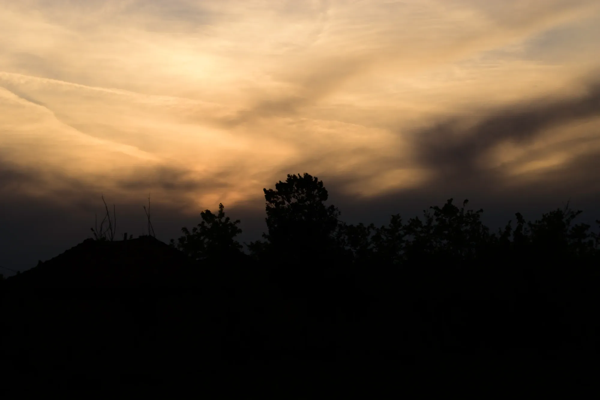 Dramatic golden evening clouds above a dark line of trees and rooftops.