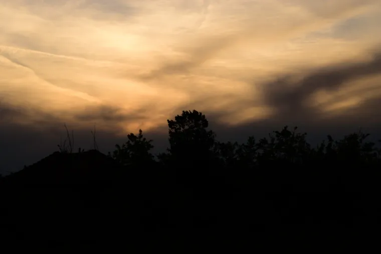 Dramatic golden evening clouds above a dark line of trees and rooftops.